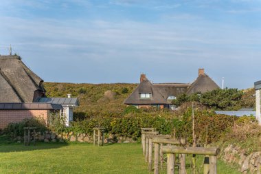 Thatched houses in landscape. Thatched-roof houses stand among greenery under a clear blue sky. The scene blends nature with coastal village charm.
