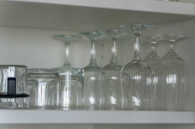 Glasses in cupboard. Wine glasses and tumblers are neatly arranged in a white cupboard. The glass reflects light, creating a clean and organized look.