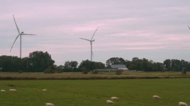 Tren penceresinden manzaralı bir manzara, gün batımında açık alanlarda rüzgar türbinlerinin açıldığını gösteriyor. Tren yeşil çayırlar ve uzak çiftlik evlerini sorunsuzca geçiyor..