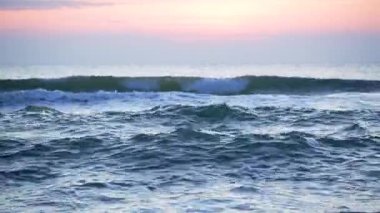 Gün batımında parlayan bir gökyüzünün altında dalgalanan okyanus dalgalarının yavaş çekim videosu. Işık sudan yansıyarak hareket eden denizin güzelliğini ve ritmini vurgular..