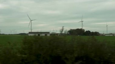 Rüzgar türbinleriyle çevrili küçük bir çiftlik ve yeşil alanlar süzülüyor. Video, modern tarım ve yenilenebilir enerjinin huzur dolu bir kırsal alanda harmanlanmasını kaydediyor..