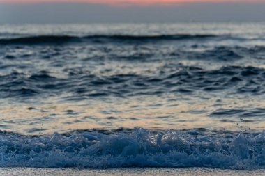Sea foam splashes at the waters edge during sunset. The fading light reflects on the rippling surface.