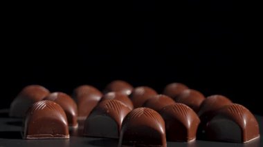 Çikolatalar yakın çekimde. Zarif çikolatalı pralinler stüdyo ışığı altında döner, parlak yüzeyler ve ince detaylar ortaya çıkar. Zengin desenli kaliteli bir şekerleme..