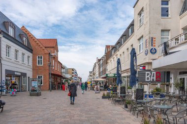 Almanya Sylt 2 Ekim 2025. Şehir alışveriş caddesi manzarası. İnsanların yürüdüğü ve kafelerin ziyaretçilere açık olduğu parlak bir sokak sahnesi. Samimi binalar ve mavi gökyüzü hoş bir bayram havası yaratır..