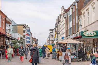 Almanya Sylt 2 Ekim 2025. Turistler ve yerliler restoranlar ve butiklerle dolu bir kasaba caddesi boyunca yürüyorlar. Açık hava tabloları ve mağaza tabelaları gevşek bir deniz manzarasını yansıtıyor.
