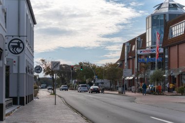 Almanya Sylt 2 Ekim 2025. Bir sahil kasabasındaki bir sokak sahnesinde bulutlu bir gökyüzünün altında trafik ve yayalar görülüyor. Dükkanlar ve kafeler ana yolda..