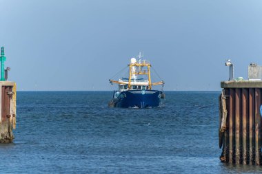 Almanya Sylt 2 Ekim 2025. Balıkçı teknesi denize doğru gidiyor. Sarı direkli mavi balıkçı teknesi limandan açık denize doğru yol alıyor. Açık gökyüzünün altında denizcilik sahnesi.