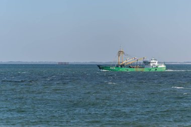 Almanya Sylt 2 Ekim 2025. Denizdeki yeşil balıkçı teknesi. Yeşil bir balıkçı teknesi sürekli olarak derin mavi sularda yüzüyor. Uzak kıyı şeridine sahip huzurlu deniz manzarası.