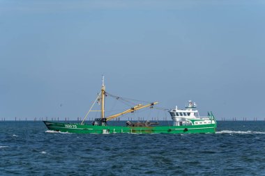 Almanya Sylt 2 Ekim 2025. Balıkçı teknesine yakın çekim. Sarı vinçleri ve mürettebatı olan yeşil balıkçı teknesinin yan görüntüsü HOO-70. Endüstriyel balıkçılık ekipmanlarını gösteren ayrıntılı deniz sahnesi.