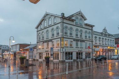 Almanya Sylt 27 Ekim 2025. Alacakaranlıkta köşe bina. Yağmurlu bir akşamda Marin Oteli 'nde parlayan camlar ve kaldırımlarda yansımalar. Ilık ışıklar, gri gökyüzüyle tezat oluşturuyor.