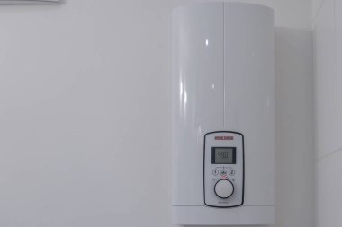 Almanya Sylt 26 Ekim 2025. Duvarda elektrikli su ısıtıcısı var. Modern dijital su ısıtıcısı beyaz bir banyo duvarına monte edildi. Temiz ve minimalist ev aletleri kurulumu.