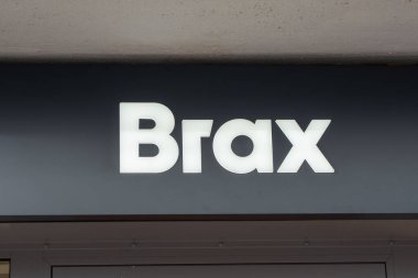 Almanya Sylt 27.10.2025. Karanlık bir cephede aydınlatılmış Brax mağaza logosunun yakın çekimi. Basit beyaz harfler bir çıkıntının altında göze çarpar.