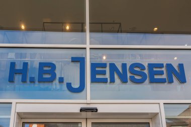 Almanya Sylt 27.10.2025. Mavi H.B. Jensen mağazasının logosu cam bir vitrinde ve binaların yansımaları var. Bir alışveriş bölgesinde modern perakende tasarımı.