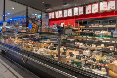 Almanya Sylt 27.10.2025. Şarküteride peynir tezgahı ve cam altında çeşitli peynir çeşitleri. Fiyat etiketleri ve örnekleri parlak iç aydınlatma ile çekici bir şekilde görüntülenir.