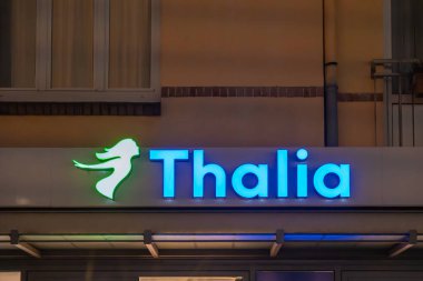 Almanya Sylt 27 Ekim 2025. Bina duvarında mavi ve yeşil ışıkları olan parlayan bir Thalia mağazası tabelası. Kitapçı logosu geceleri göze çarpıyor..