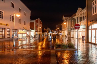Almanya Sylt 28 Ekim 2025. Yağmurdan sonra altın sokak lambalarının altında sessiz bir yaya caddesi parlar. Islak asfalt çevredeki dükkanlardan ve evlerden gelen sıcak ışıkları yansıtıyor..