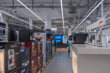 Almanya 31 Ekim 2025. Kahve makineleri ve televizyonlarla dolu bir elektronik mağazasının içindeki koridor. Parlak ışıklandırma çeşitli marka ve modern aygıtları vurgular.