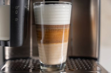 Kadehteki katmanlı latte macchiato 'nun yakın çekimi. Yumuşak süt köpüğü espresso şeridini taçlandırır..