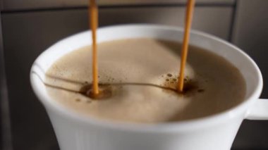 İkiz espresso akıntıları kalın krema şeklinde beyaz bir kaba düşer. Altın kurdeleli pürüzsüz çıkartma.