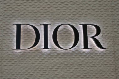 Dokulu bir duvarda aydınlatılmış DIOR logosu. Minimalist lüks markalaşma..