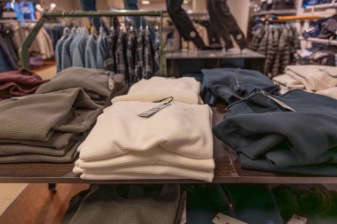 Erkek giyim masasına dizilmiş katlanmış kazak ve kapüşonlular. Sıcak dokular ve tarafsız tonlar sonbahar alışverişini akla getiriyor.