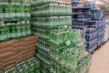 Paletlere sarılı şişelenmiş su yığınları süpermarket koridorunu dolduruyor. Yeşil ve mavi toplu içecekler depolama alanına hakim..