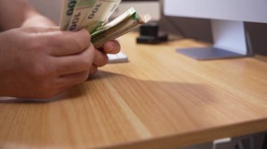 Elleri, ahşap bir ofis masasının üzerinde bir yığın euro tutar. Sahne maaş sayımı, tasarruf yönetimi veya nakit ödemeyi temsil ediyor.