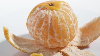 Yarım soyulmuş bir Clementine beyaz bir yüzeyde yavaşça döner. Video, narenciyenin lifli dokusuna odaklanıyor..