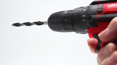 Yakın plan kablosuz matkap sürücüsü, matkap ucu ile beyaz arka planda dönüyor. Bir el tetiğe basar, stüdyonun ışığındaki halkayı ve halkayı gösterir..