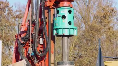 Almanya 27 Kasım 2025. Kırmızı direğe monte edilmiş yeşil bir kovan sürücüsü olan endüstriyel sondaj kulesi. Ağır ekipmanlar temel ve kazık işleri için açık havada çalışır..