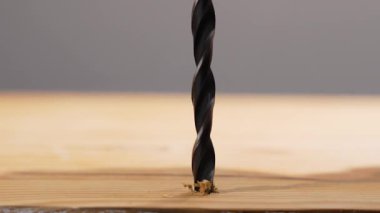 Bükme matkabı bir sonraki delik için mükemmel hizalanmış ahşap bir tahtanın üzerinde asılı duruyor. Sığ alan derinliği kesme ucunu izole eder.