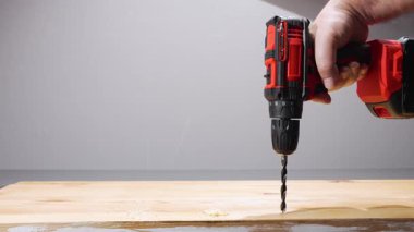 Kablosuz matkap, çam ağacına biraz bükülmüş ve temiz bir deliği tıkıyor. Talaş, tahıl ve sağlam ellerle atölyeye yakın çekim.