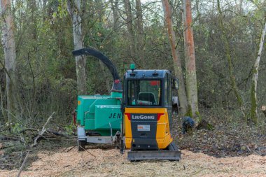 Almanya 27 Kasım 2025. LiuGong kazıcısı Jenz odun öğütücüsünün yanına park etmiş taze cipslerle dolu bir yatağın üzerine. Ormanlık alanda orman temizleme sahnesi.