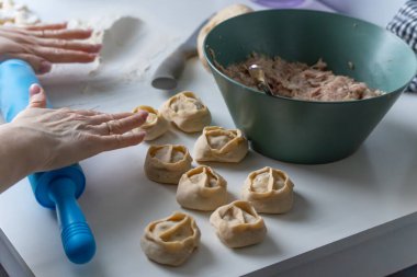 El yapımı hamur köftelerini un kaplı bir masada kıyma dolu bir kasenin yanında şekillendiren eller. Hamur mermileri, katlanmış hamur tatlısı ve parlak bir mutfakta merdane..