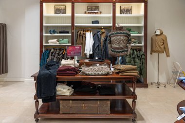 Almanya 3 Aralık 2025. Kırsal ahşap masada katlanmış süveterler, pantolonlar ve toprak renkte ceketler sergileniyor. Klasik gardırop parçalarıyla sıcacık kış moda köşesi.