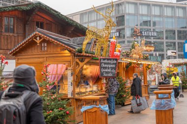 Almanya 3 Aralık 2025. Berlin 'deki bir Noel pazarında tezgahtan buhar yükseliyor ve yakınlarda müşteriler var. Altın ren geyiği süslemesi ve sıcak ışıklar sıcak bir kış havası yaratır..