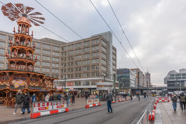 Almanya 3 Aralık 2025. Berlin Alexanderplatz kışın Noel pazarı piramidi, tramvay rayları ve yayalar ile. İnşaat bariyerleri ve kablolar işlek şehir meydanını çerçeveliyor.