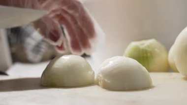 Eldivenli bir el soyulmuş bir soğanı bıçakla kesme tahtasına keserken sabitler. Çorba, sos ve kıyma için mutfak hazırlığı..