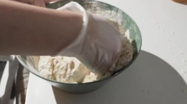 Eldivenli eller, parlak güneş ışığı altında un tozlu bir kasede yapışkan hamur yoğurur. Ev yapımı ekmek ya da pizza tabanı için yakın çekim pişirme işlemi.