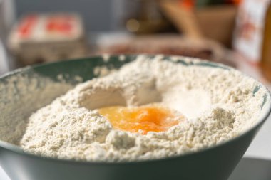 Çiğ yumurta, ev yapımı hamura hazır bir karıştırma kabında un kuyusuna kırılır. Sıcak bir mutfakta malzemeler pişiriyorum..