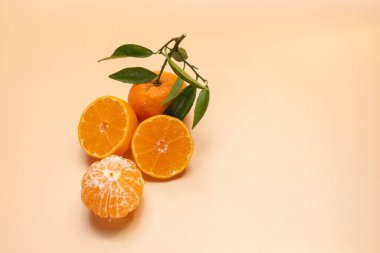 Turuncu yarımlar ve bej arka planda yeşil yapraklı soyulmuş bir mandalina. Taze turunçgiller, sağlıklı atıştırmalıklar ve fotokopi alanı..