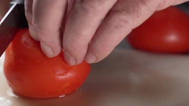 Domatesi doğrayıcı bir tahta üzerinde düzgün dilimleyen ellerin yakın çekimi. Salataya, sandviçe ya da yemek pişirme sahnelerine hazırlar..