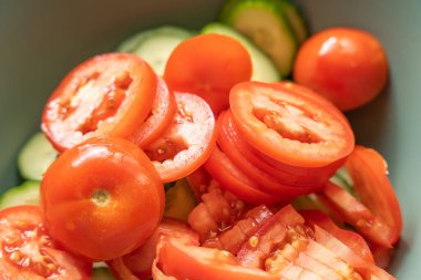 Salatalıklı mermilerin üstüne domates dilimleri yığılmış. Sulu kırmızı yüzeyler ışıkta parlıyor, basit, renkli bir sebze salatası sergiliyor..