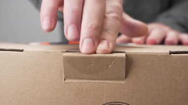 Ellerin karton bir kutuyu açtığı yakın çekim videosu. Klip, ambalaj ve beklenti odaklı bir boks sürecinin ilk adımını gösteriyor.