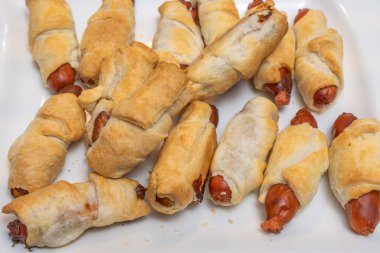 Beyaz bir tabağa yerleştirilmiş altın puf böreği sosisi. Klasik parmak yemekleri partiler, açık büfe ya da günlük toplantılar için idealdir..