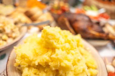 Patates püresi ve arka planda yiyecek. Kremalı patates püresi, arka planda geleneksel yemekler olan bir tabakta servis edilir. Ev yapımı yemek ve sıcak yemek atmosferini ön plana çıkaran konforlu yemek sahnesi.
