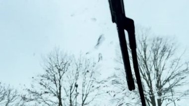 Arabanın ön cam silecekleri kış havasında camda hareket eder, aracın içinden görülürler. Bulanık ağaçlar ve soğuk ışık kar koşullarında sakin ve dengesiz bir sürüş atmosferi yaratır..