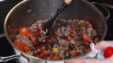Doğranmış domates ve domates ezmesi bir tencerede doğranmış ete eklenir. Yakın plan çekimde taze malzemeler ve zengin bir acı biber sosunun başlangıcı vurgulandı.