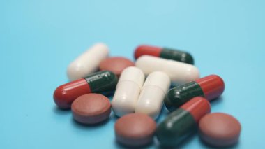 Mavide gruplandırılmış çeşitli haplar. Mavi arka planda gruplandırılmış çeşitli kapsüllerin ve tabletlerin yakın çekim videoları. Temiz kompozisyona sahip ilaç ve sağlık konsepti.