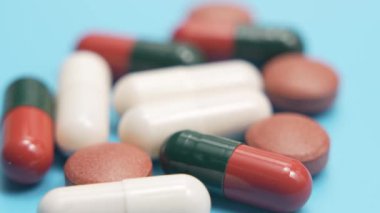 Mavi arka planda çeşitli haplar var. Mavi arka planda çeşitli kapsüllerin ve tabletlerin yakın plan videoları. Sığ alan derinliğine sahip ilaç ve sağlık konsepti.